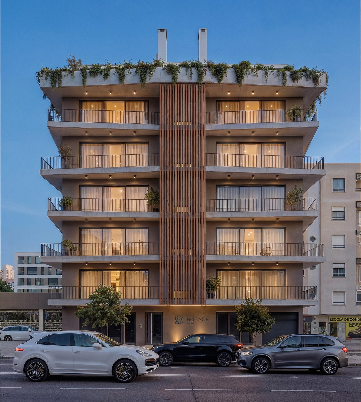 Edifício Bocage façade at dusk, with lit interiors and planting on the roof.