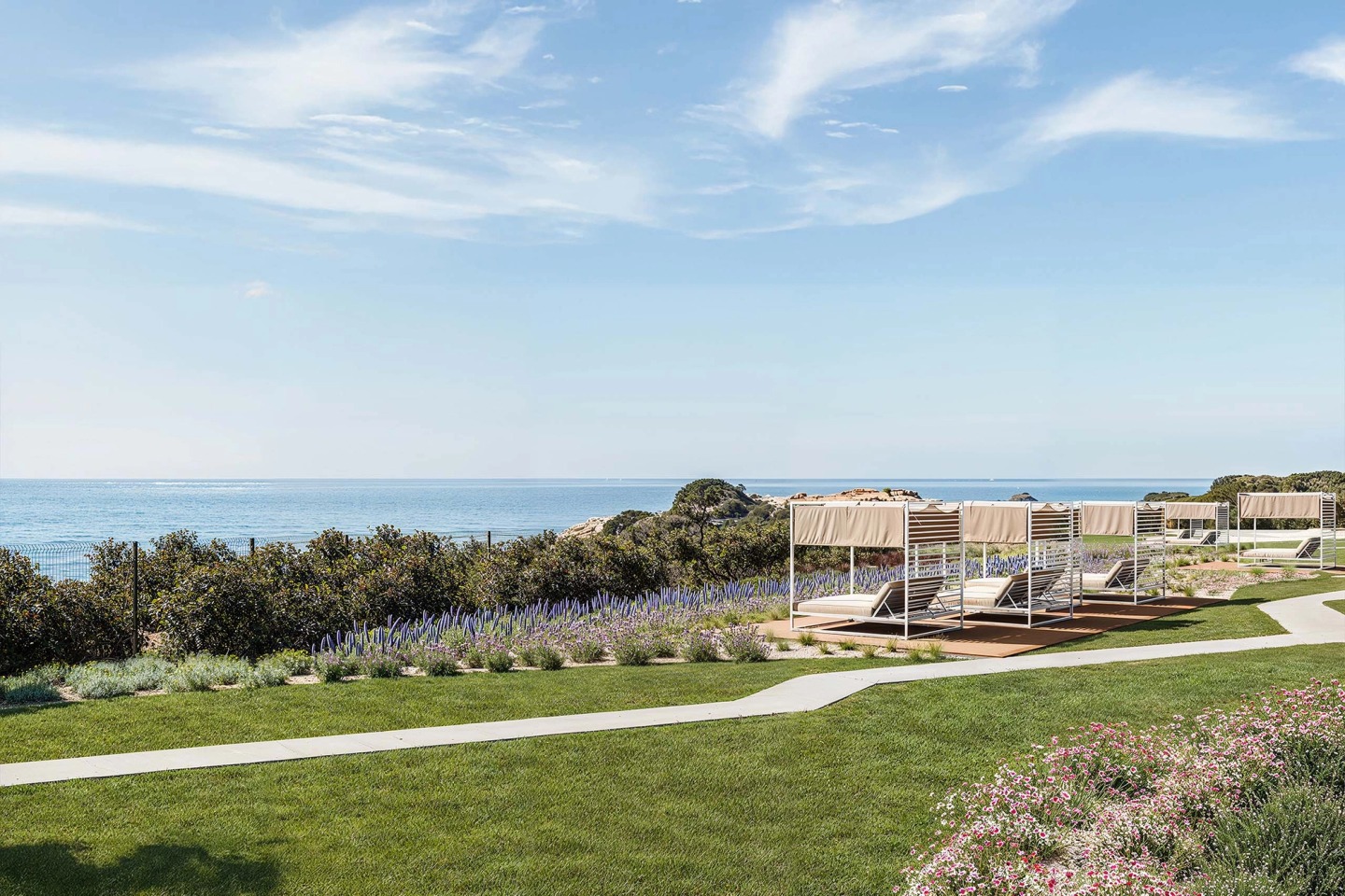 Hotel garden with cabanas and sun loungers at the edge of the cliff, the sea beyond.