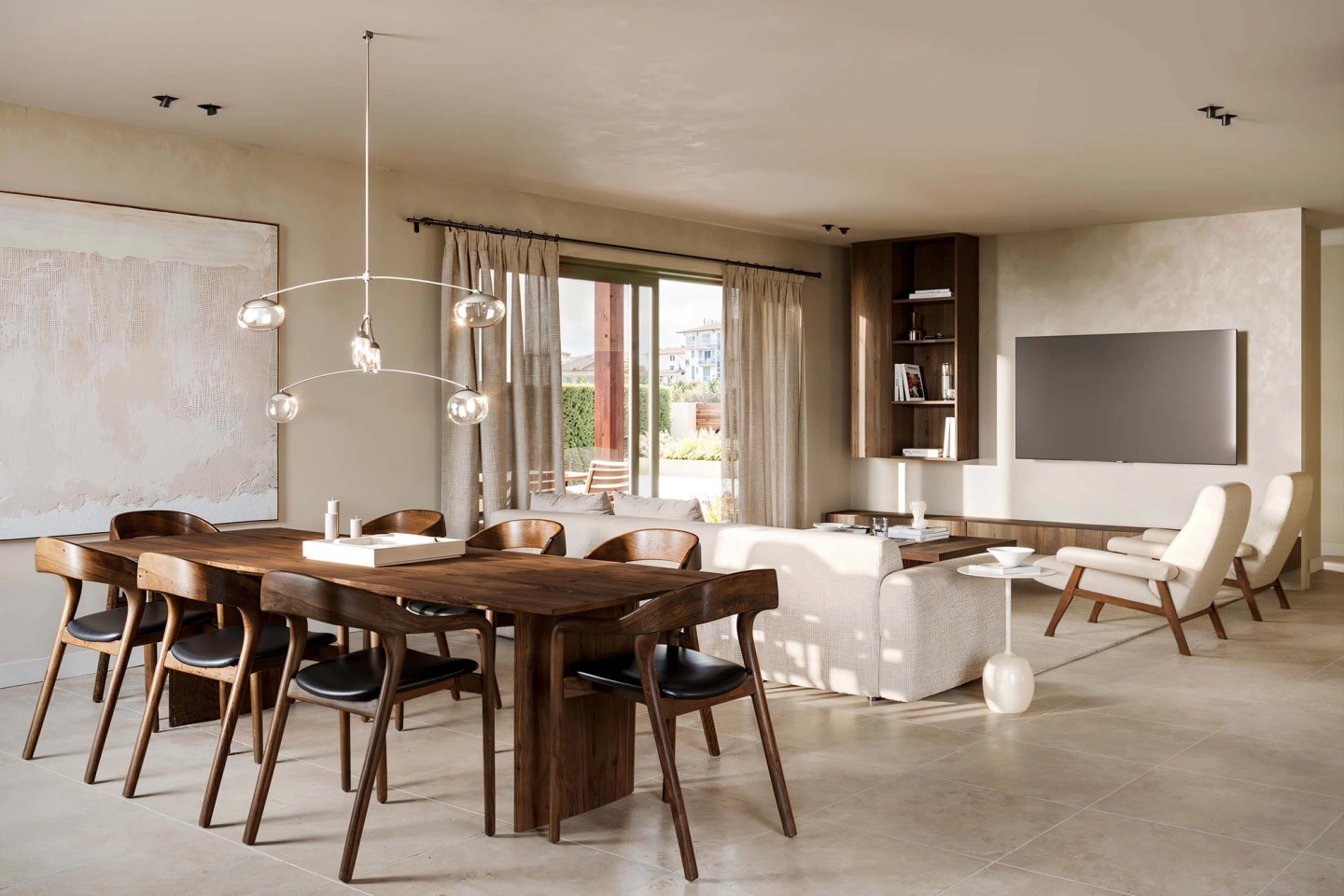 Living room with a timber dining table, white sofa and glass pendant light, opening onto the garden.