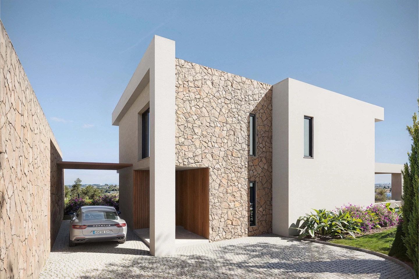Entrance to a Pearl Villas house with a stone wall, carport and a parked car.