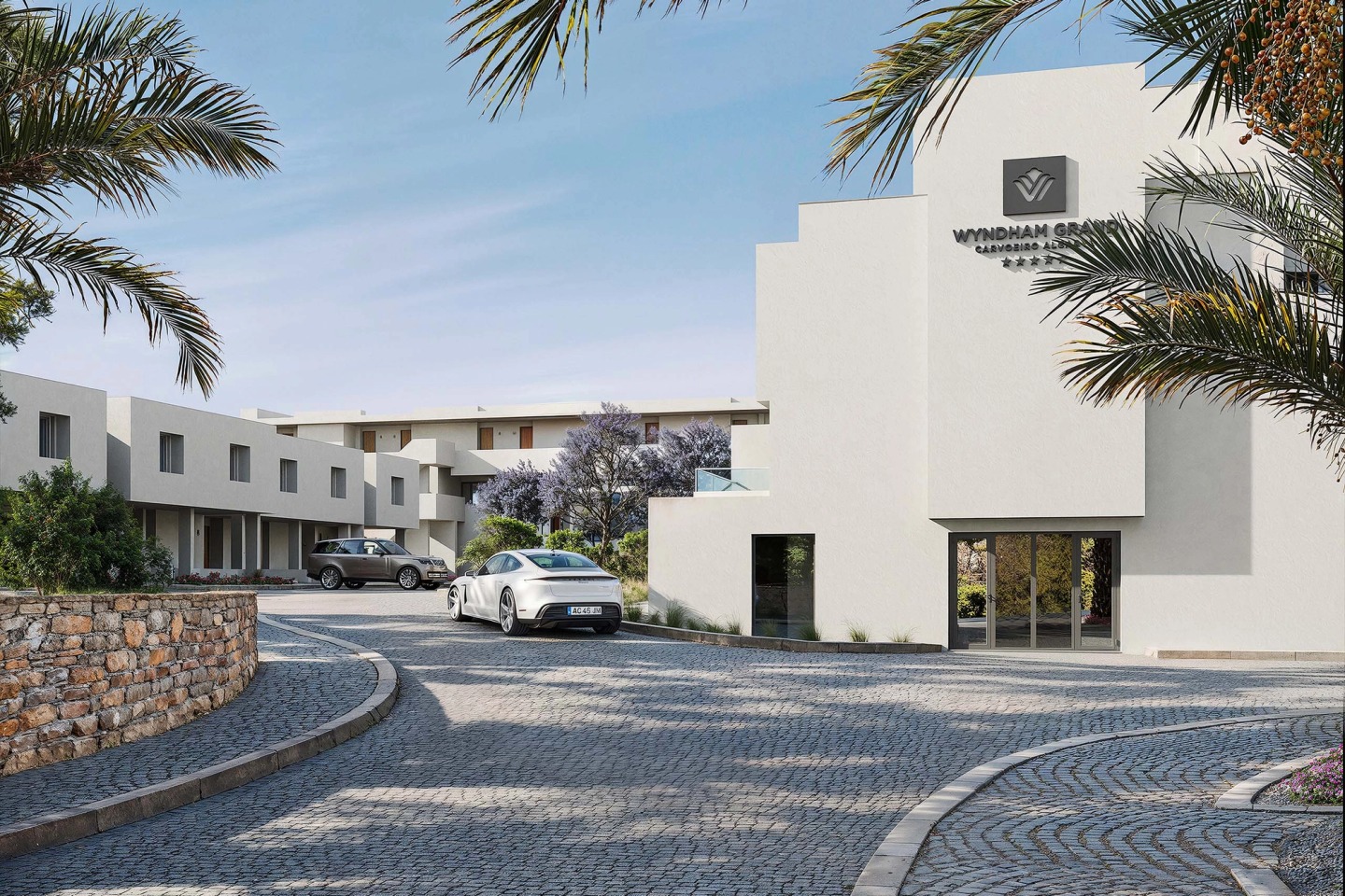 Entrance to the Wyndham Grand Carvoeiro Algarve hotel, with white buildings, palm trees and Portuguese paving.