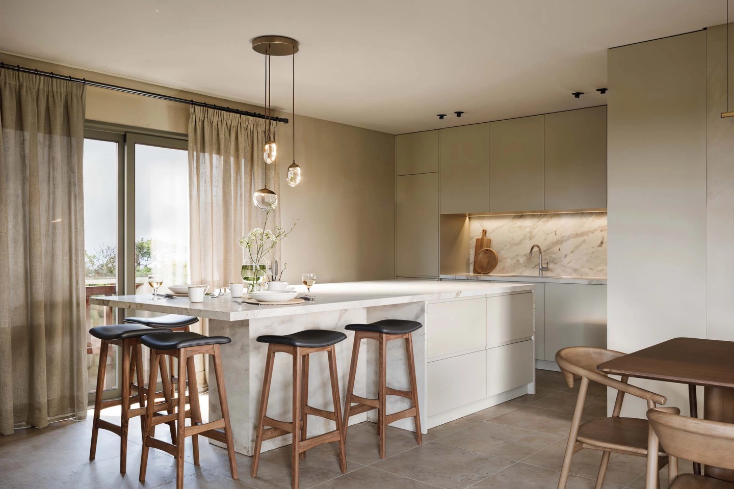 Kitchen with a stone island, tall timber stools and glass pendant lamps.