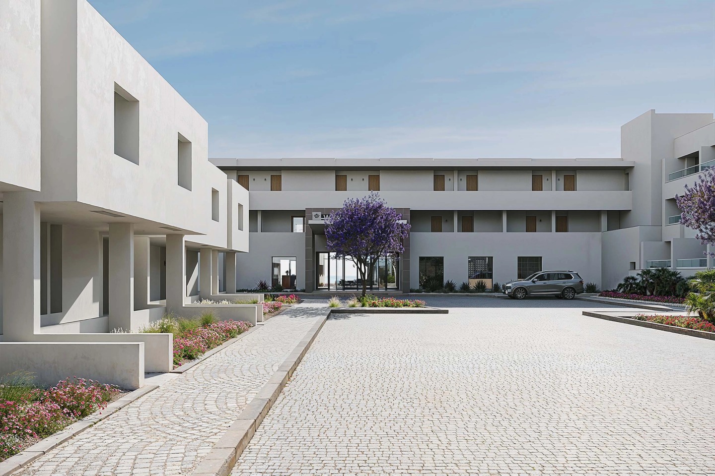 Arrival court of the Wyndham Grand Carvoeiro with paving, a flowering jacaranda and the reception beyond.