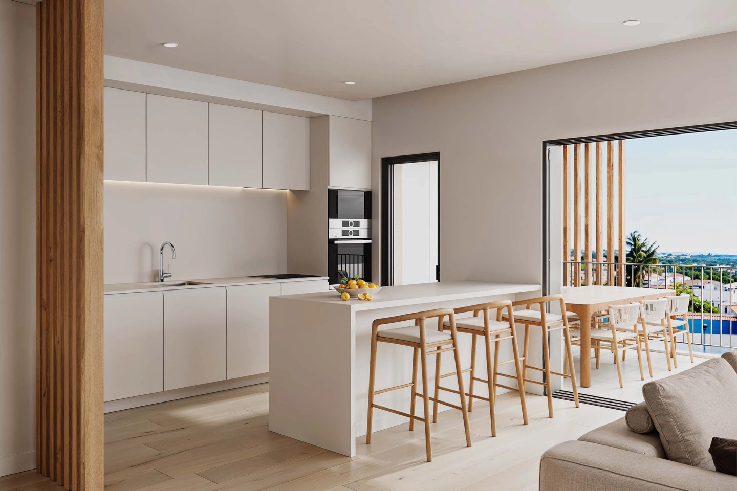 White kitchen with an island and timber stools, opening onto a balcony with a view.