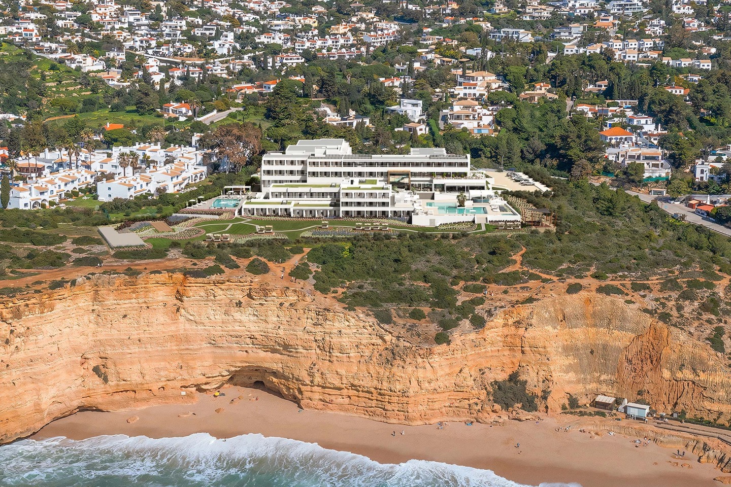 Aerial view of the Wyndham Grand Carvoeiro on top of the cliff, with the beach and sea below and Carvoeiro village behind.