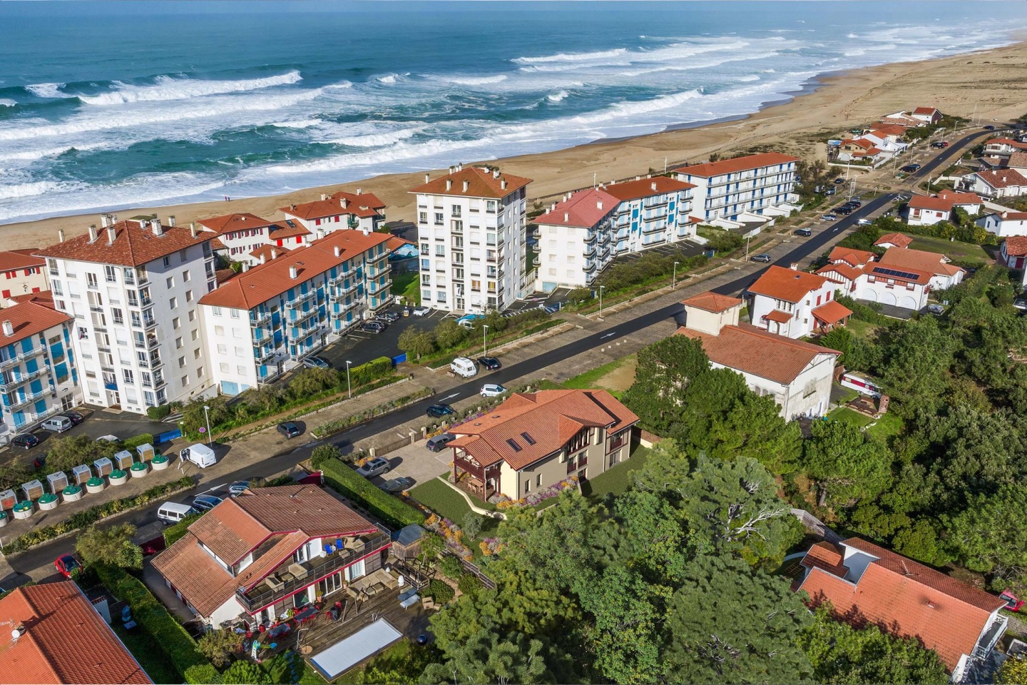 Aerial view of Hossegor with the house among trees and red roofs, the beach and Atlantic waves beyond.