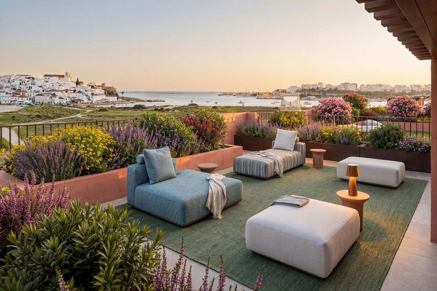 Terrace with sofas and flowering plants overlooking Ferragudo village and the Arade river at sunset.