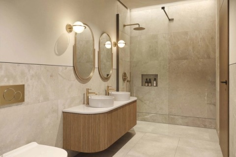 Bathroom with a curved fluted-timber vanity, oval brass mirrors and a light stone shower.