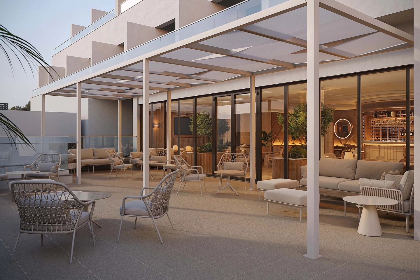 Bar terrace under a pergola at dusk, with outdoor sofas and chairs and the lit interior behind.
