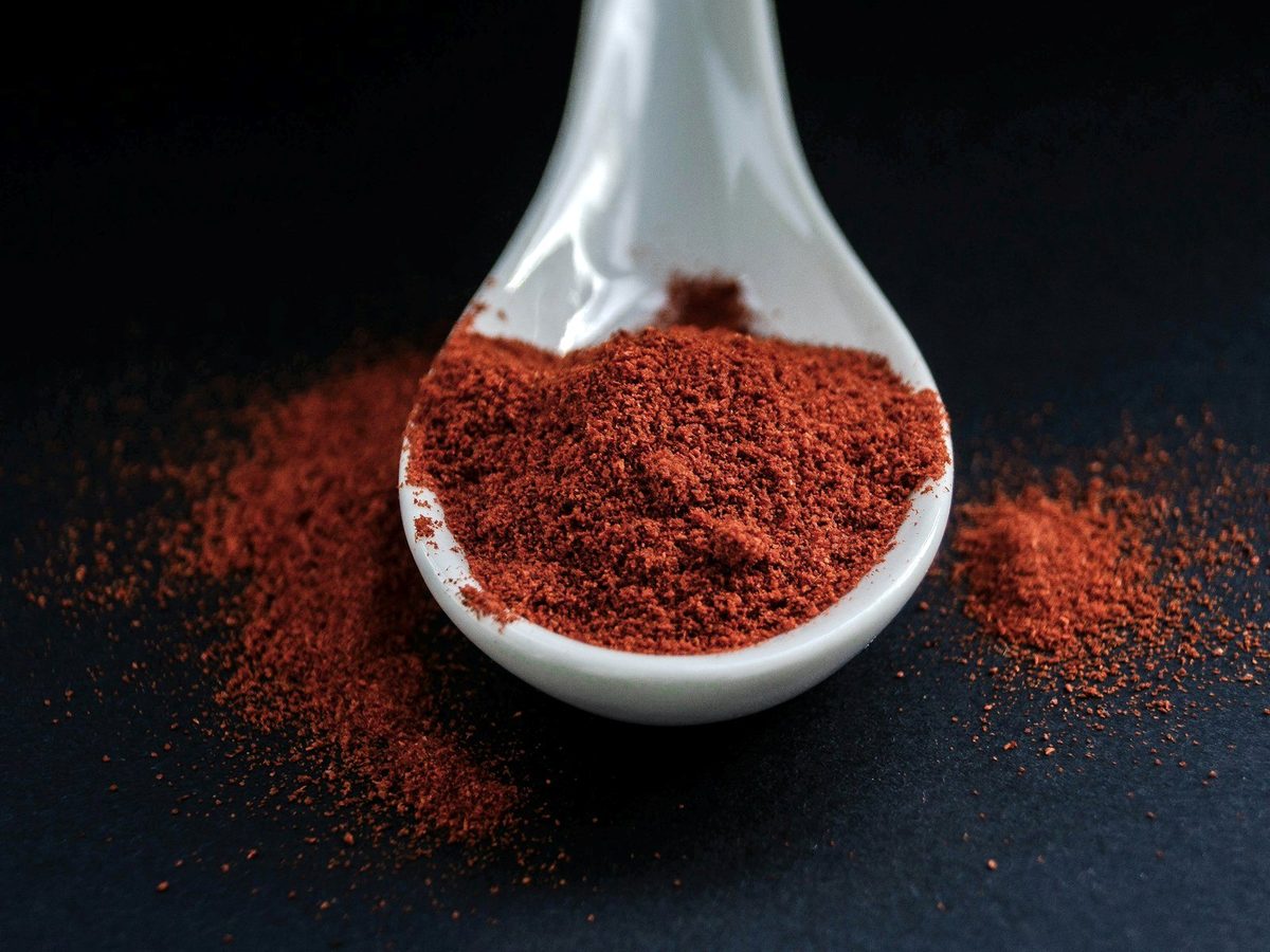 Red chili powder heaped on a white spoon on a dark background.