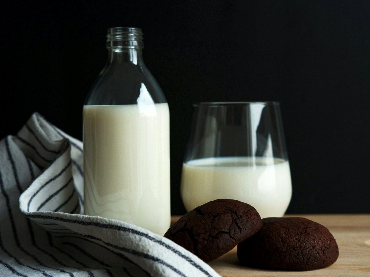 A glass bottle and a glass of milk on a wooden table with two cookies.