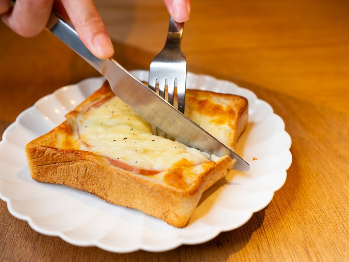 A homemade croque-monsieur with golden melted cheese on a scalloped plate, cut with a knife and fork.