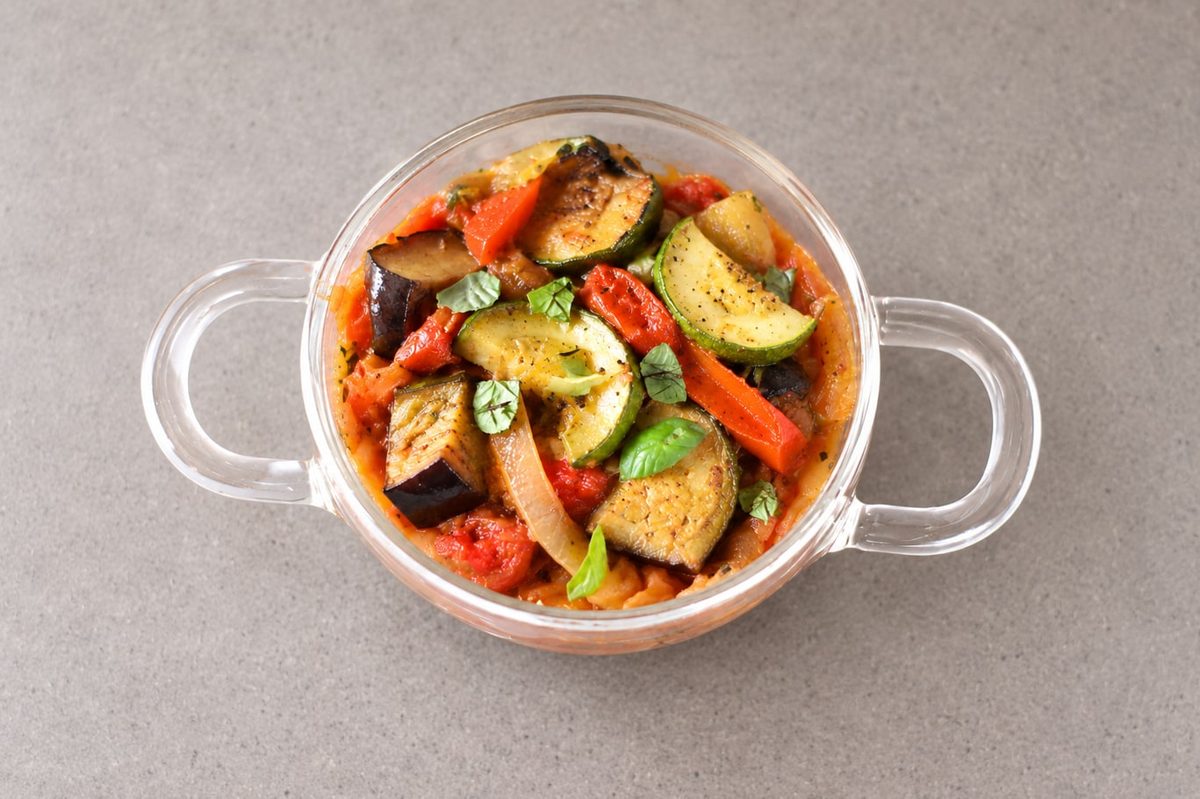 Ratatouille of zucchini, eggplant, red pepper and tomato with fresh basil in a glass bowl.