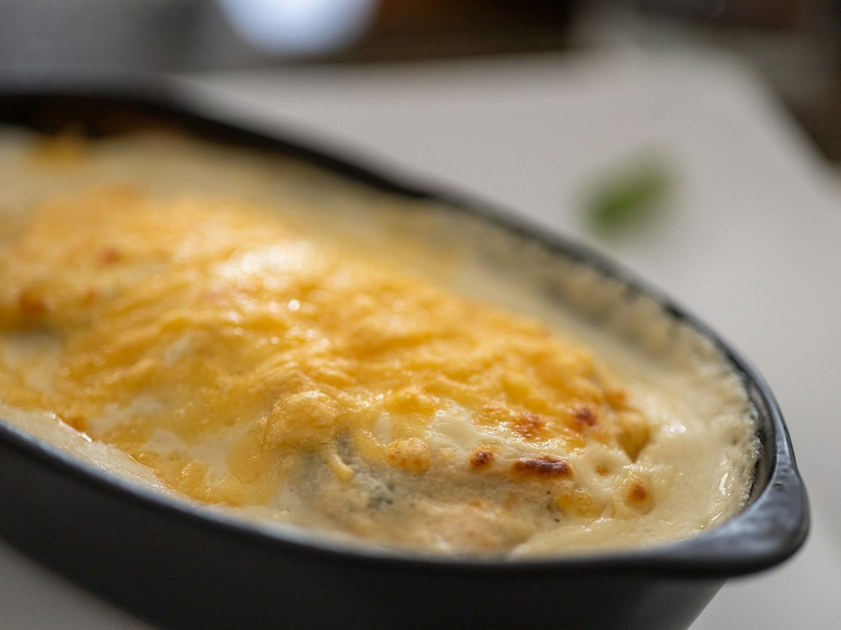 A gratin of endives wrapped in ham under a golden, bubbling cheese sauce in a black dish.
