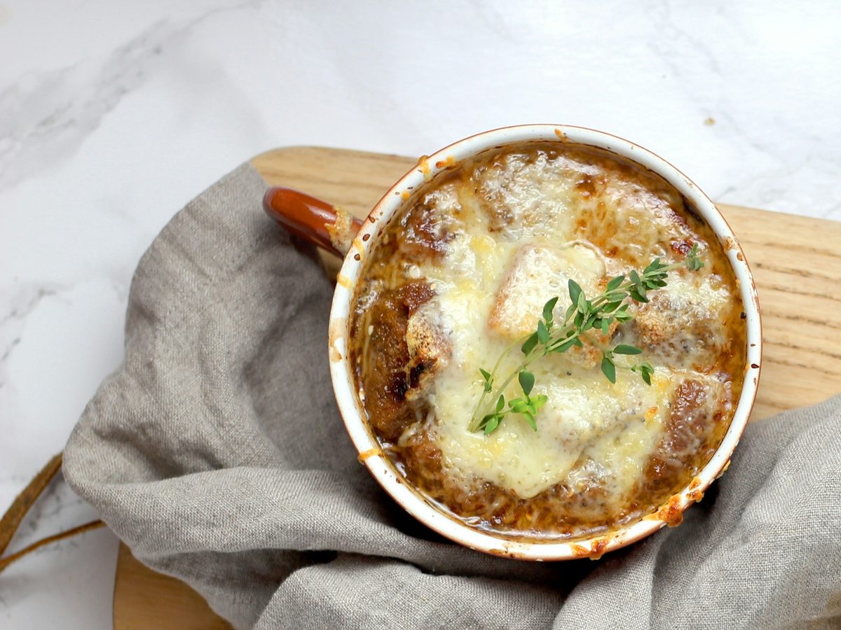 French onion soup in a crock, covered with melted, browned cheese and a sprig of thyme.