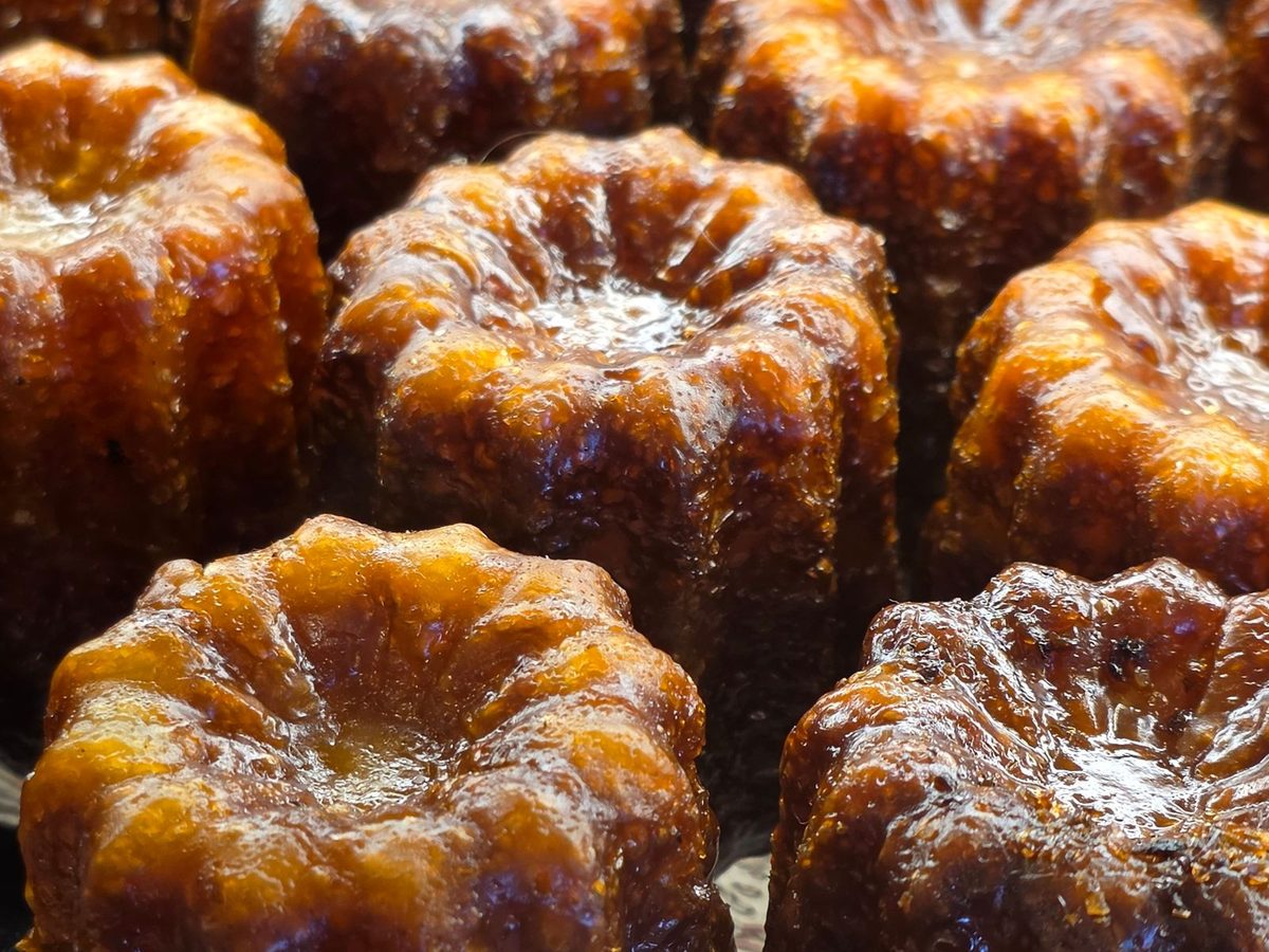 Close-up of glossy, caramel-brown cannelés with deep ridges, lined up in rows.