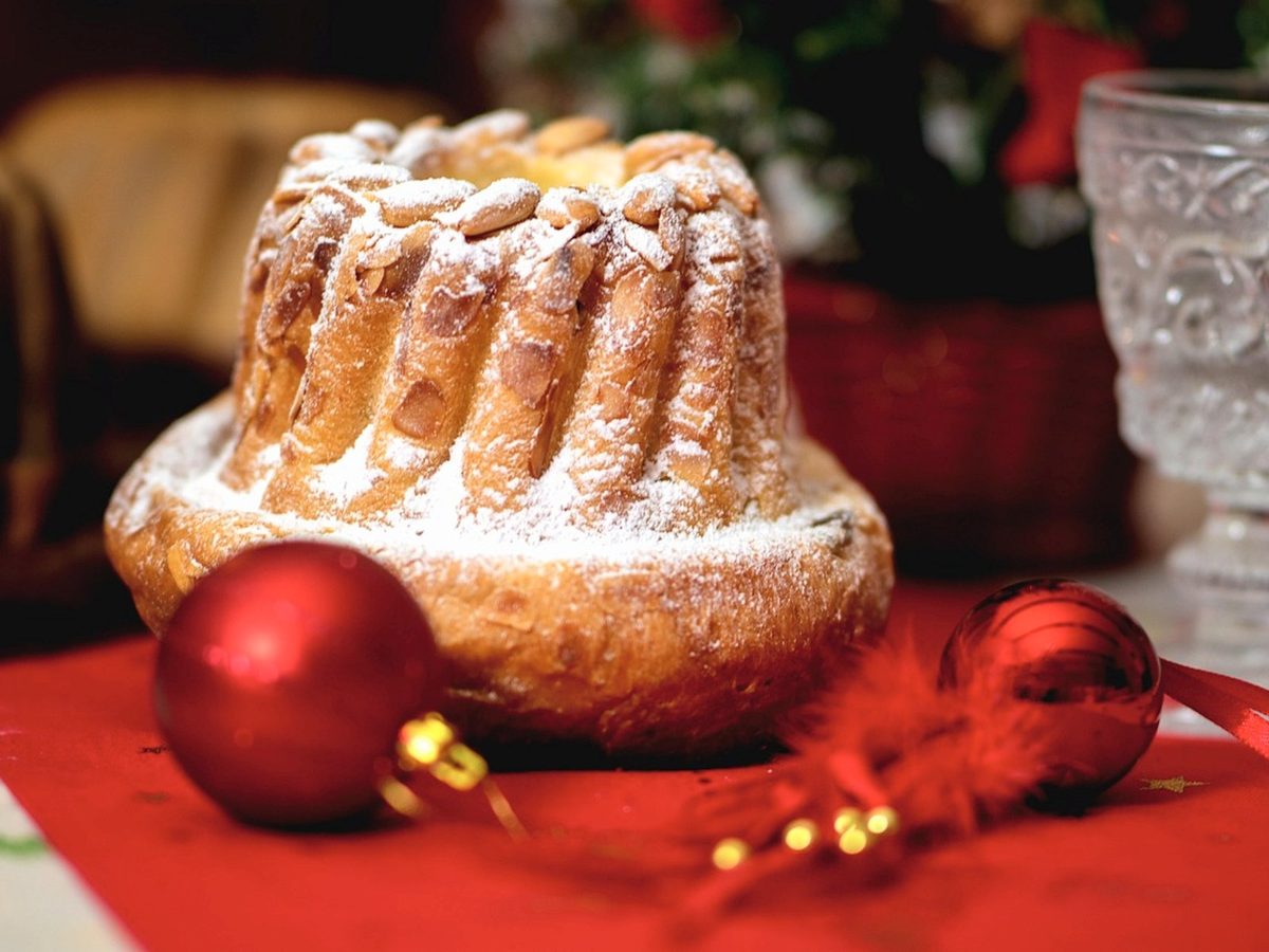 A tall fluted kougelhopf topped with almonds and dusted with icing sugar, next to red Christmas baubles.