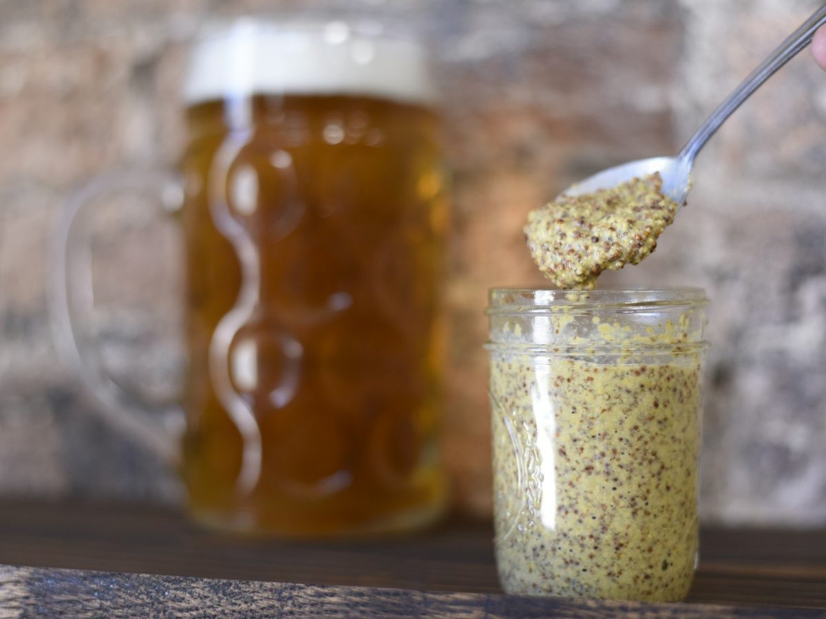 A spoon lifting grainy mustard out of a glass jar.