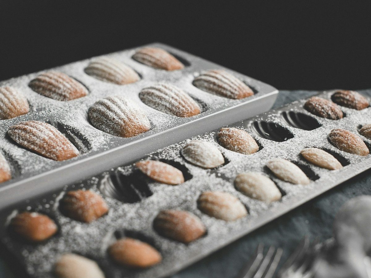 Two metal madeleine pans filled with baked madeleines dusted with icing sugar.