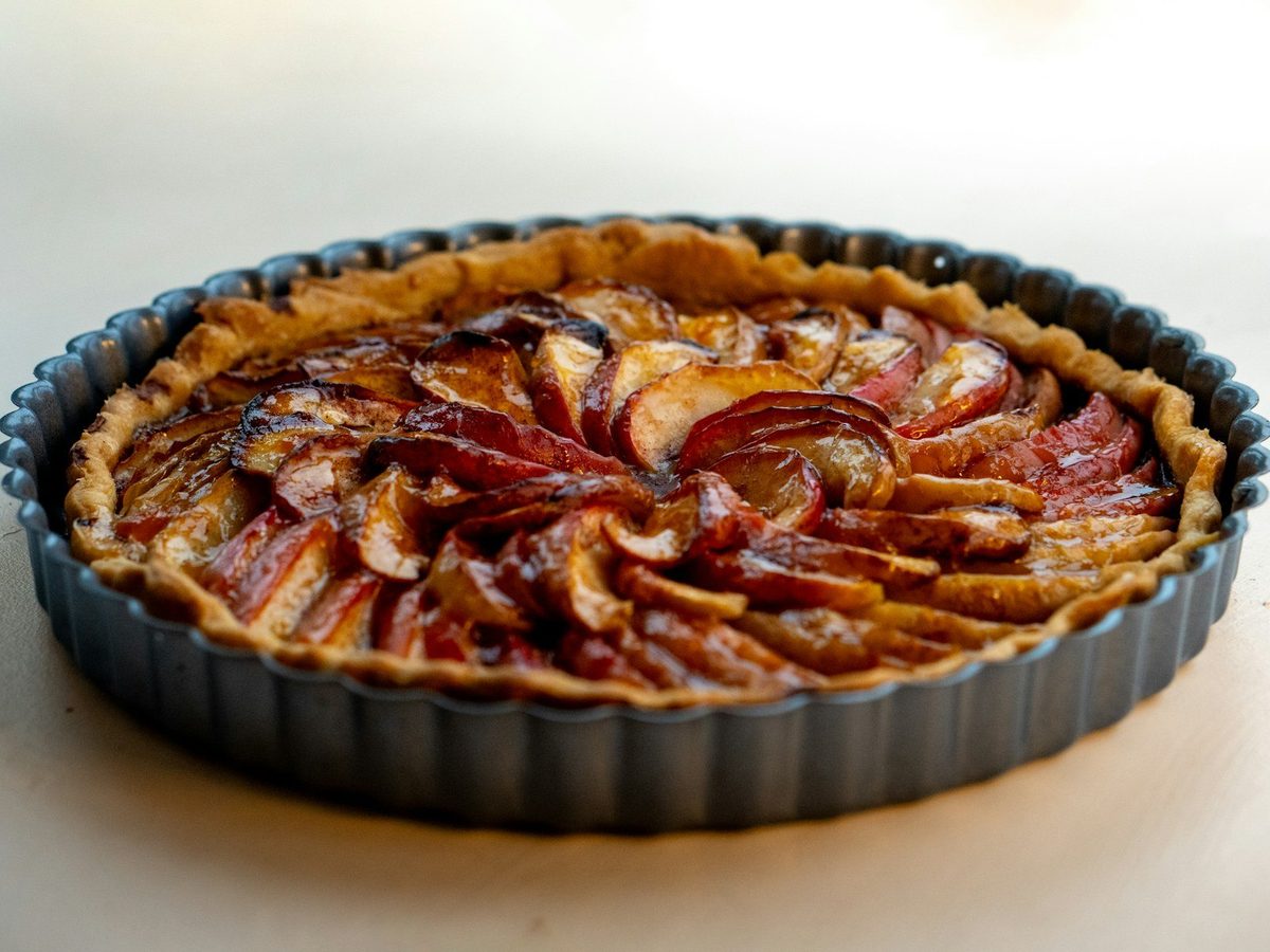 A fruit tart baked in a dark fluted metal tart pan.