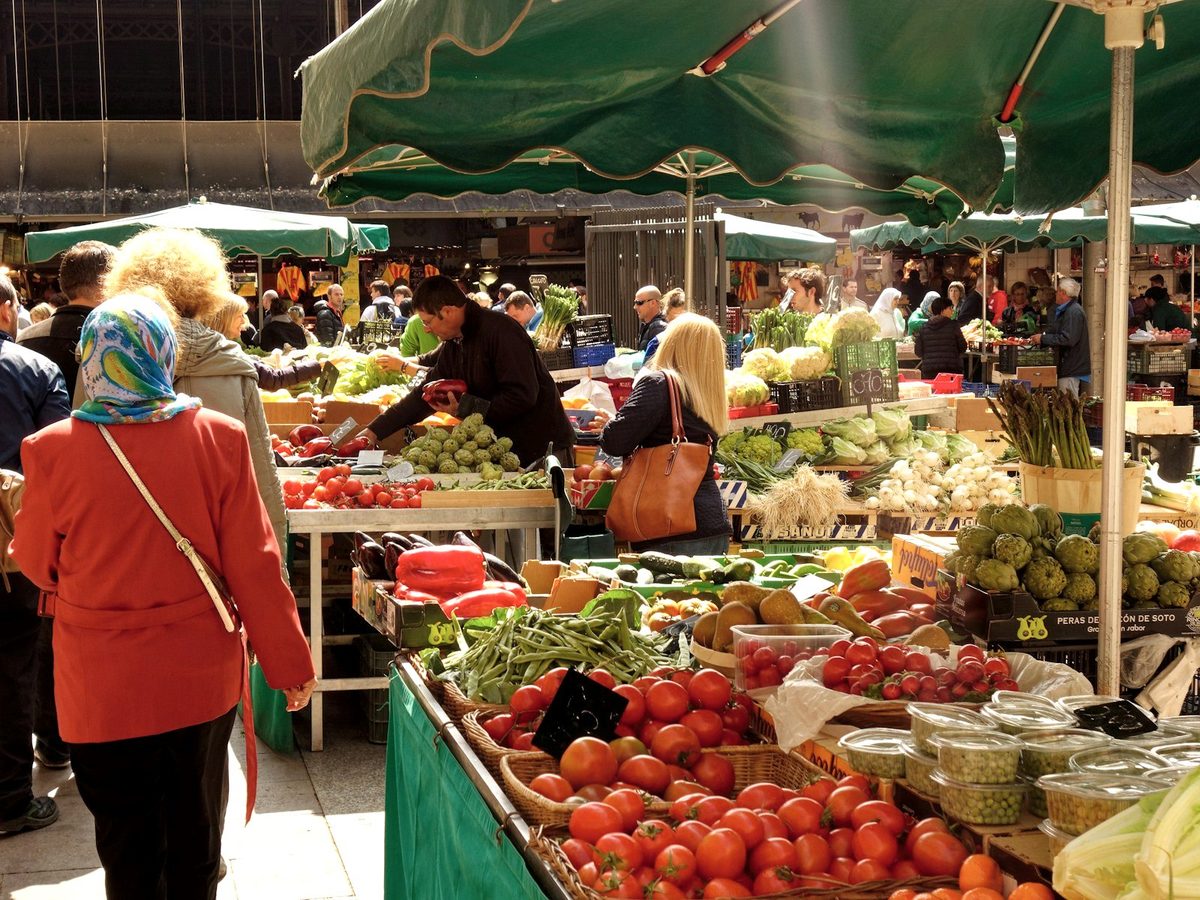 A busy French outdoor market with stalls of vegetables and fruit under green umbrellas.