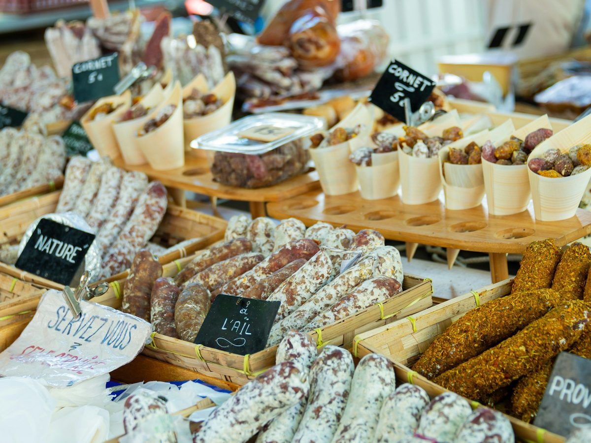 Dry sausages and saucissons laid out at a French market stall with handwritten labels.