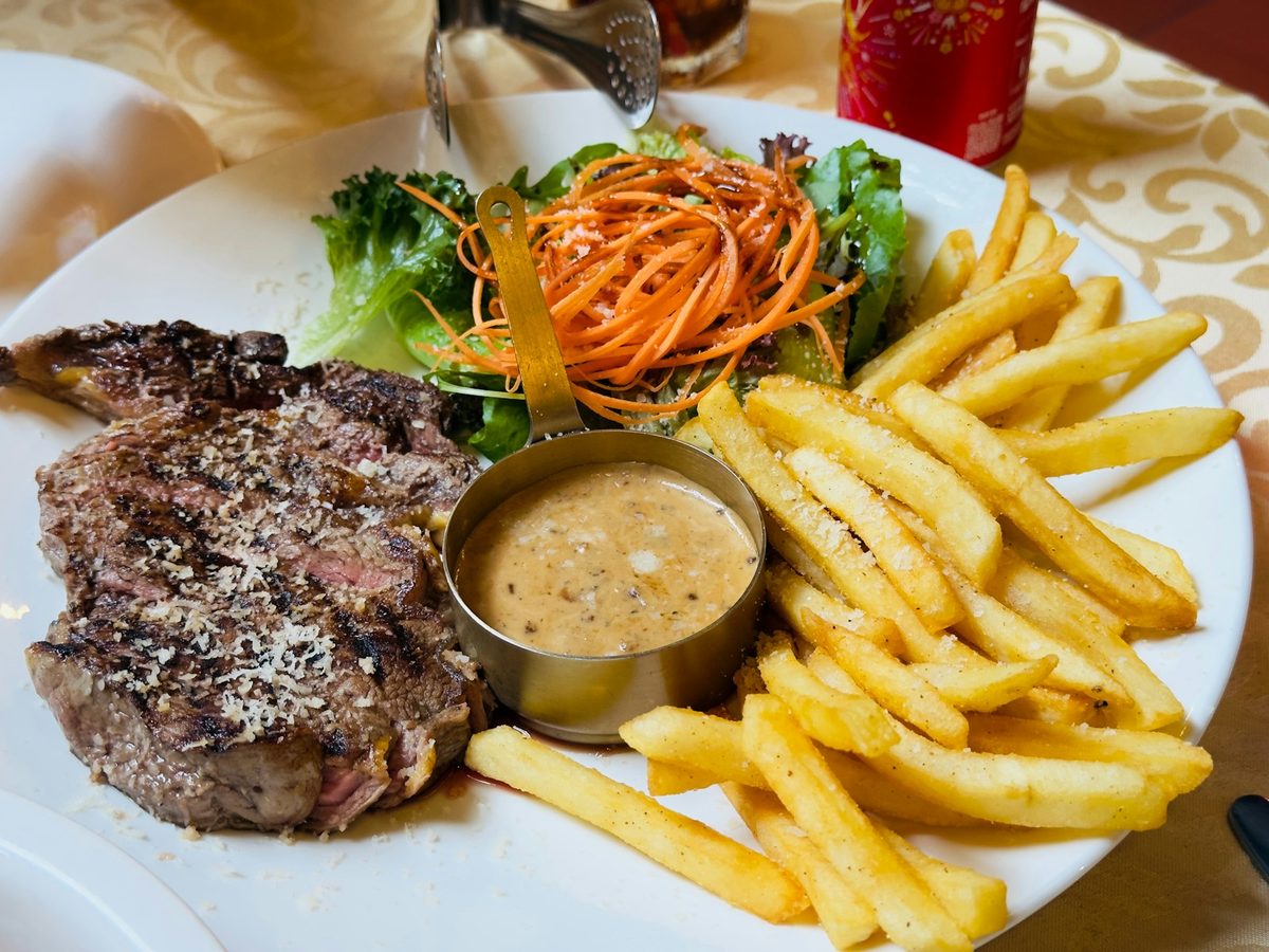 Grilled steak with a small pot of peppercorn cream sauce, fries and salad.