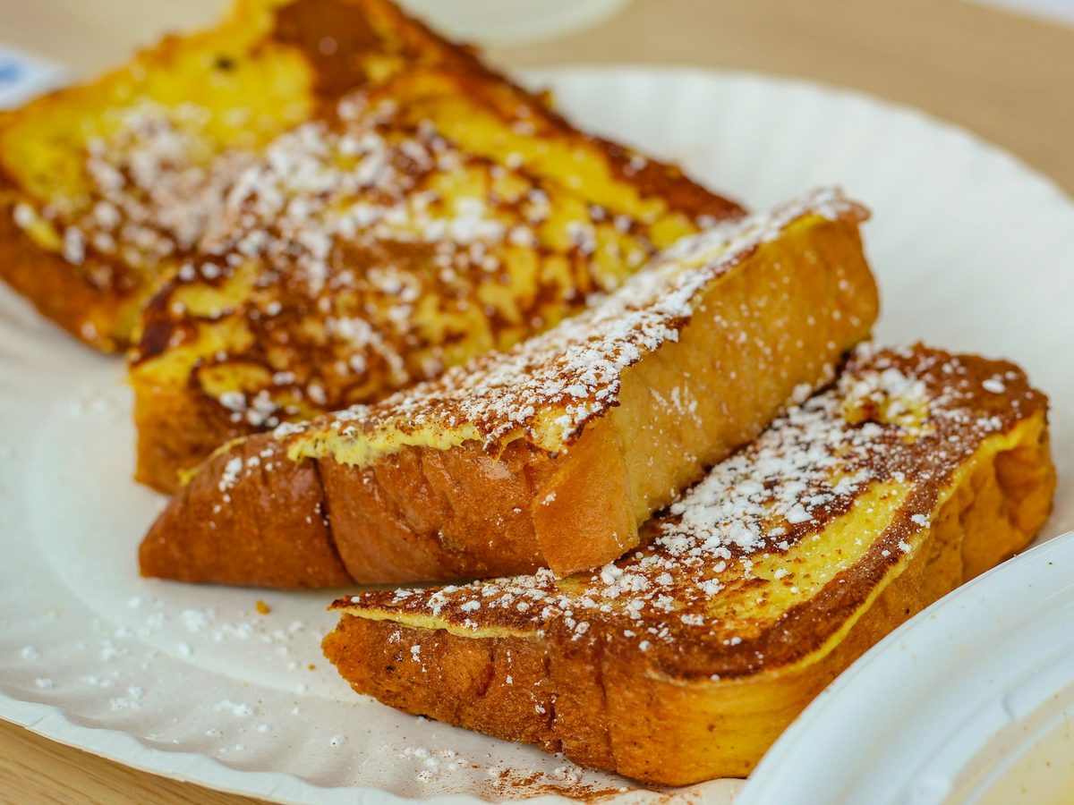 Thick slices of golden pan-fried French toast dusted with icing sugar on a white plate.