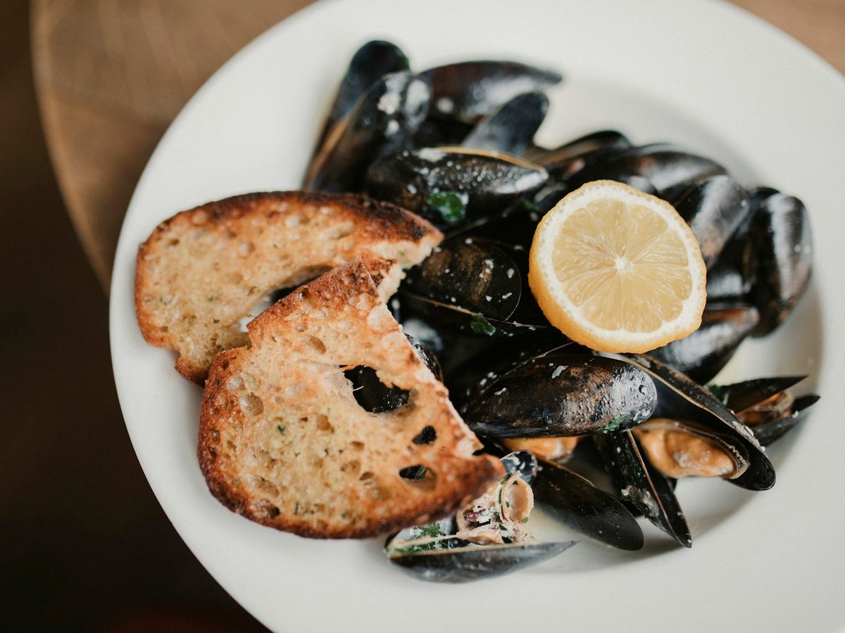 A plate of steamed mussels with toasted bread and half a lemon.