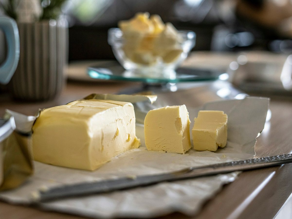 A block of butter with a few slices cut off, on paper on a kitchen counter.