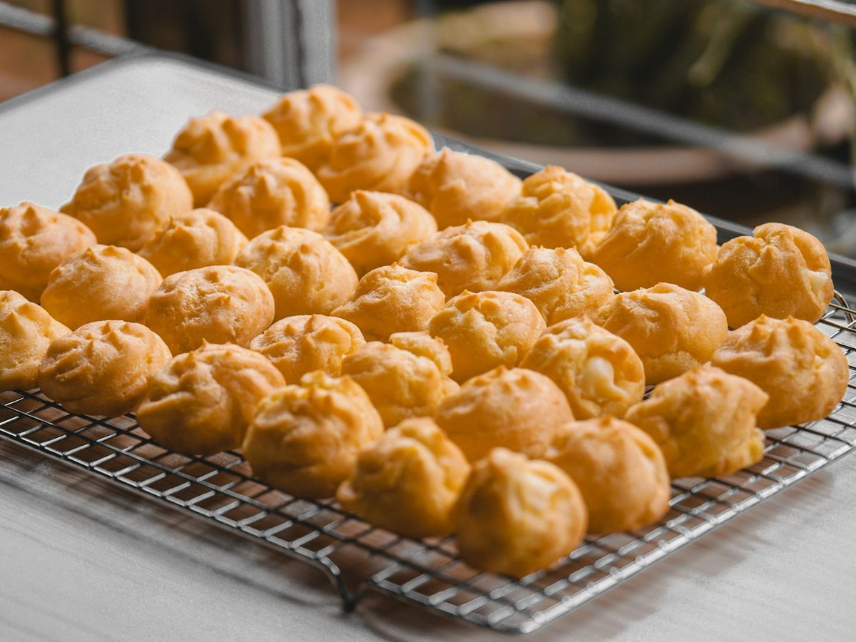 Rows of golden, freshly baked choux puffs cooling on a wire rack on a kitchen counter.