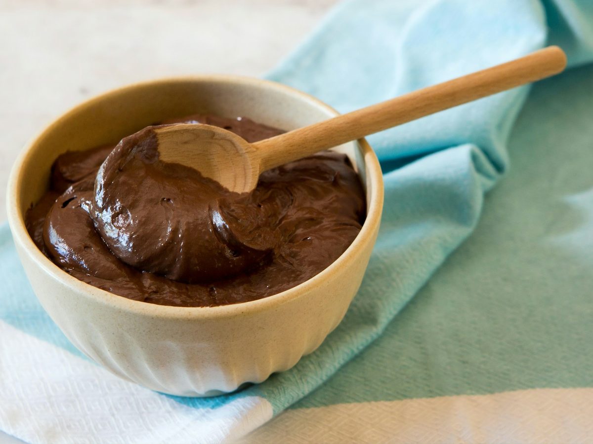 A bowl of dark chocolate mousse with a wooden spoon resting in it, on a blue and white cloth.