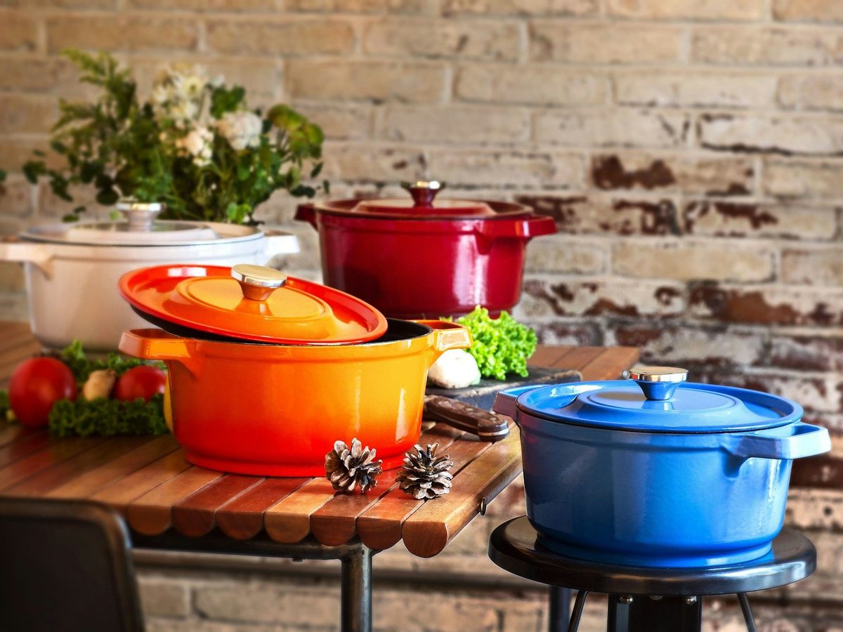 Enamelled cast-iron cocottes in red, orange, white and blue on a wooden table.