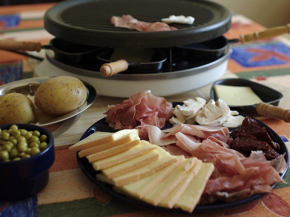A round raclette grill with small pans, potatoes and a platter of cheese and charcuterie.