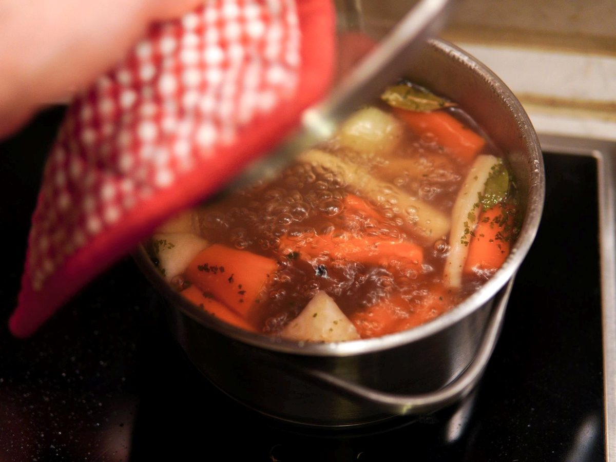 A pot of clear broth with carrots, leeks and turnips simmering on the stove.