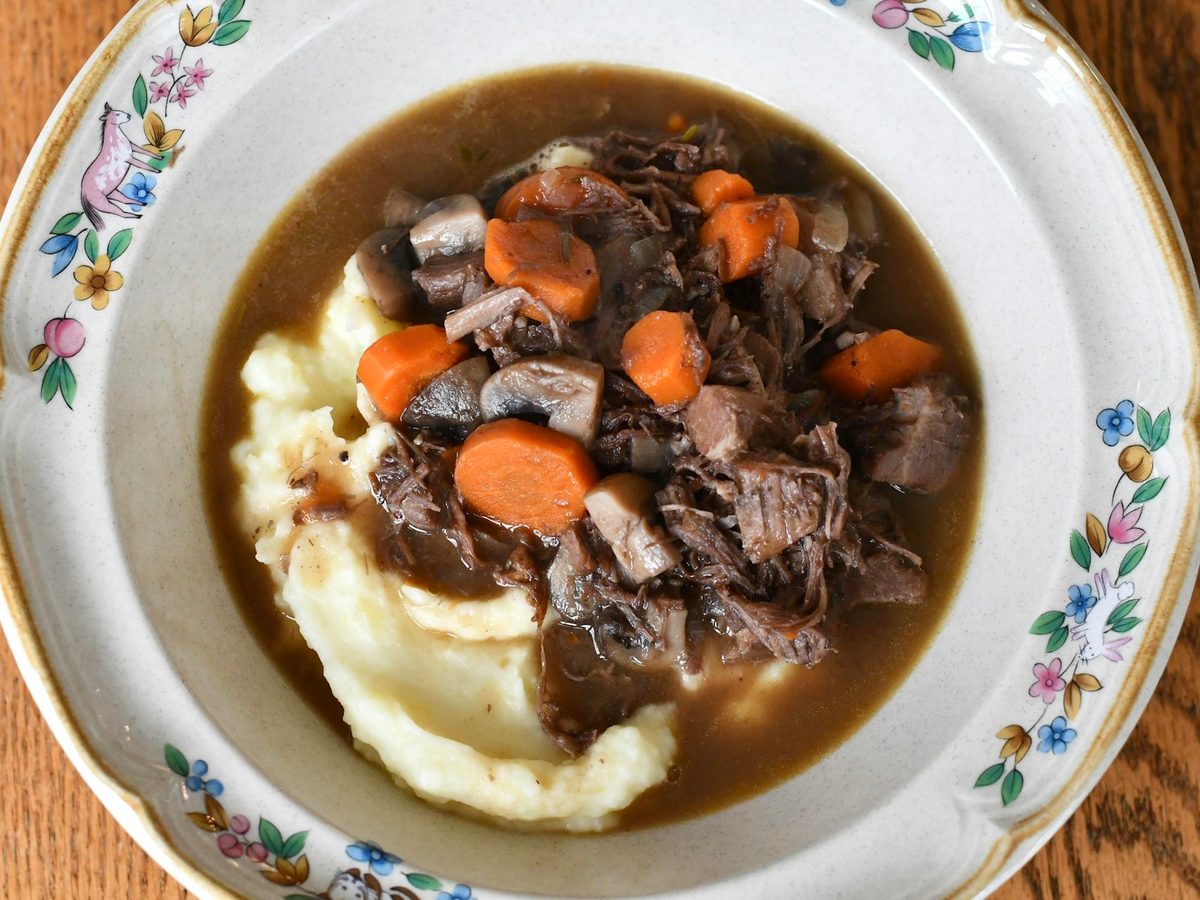 Beef bourguignon with carrots and mushrooms in a dark wine sauce, served over mashed potatoes on a floral plate.