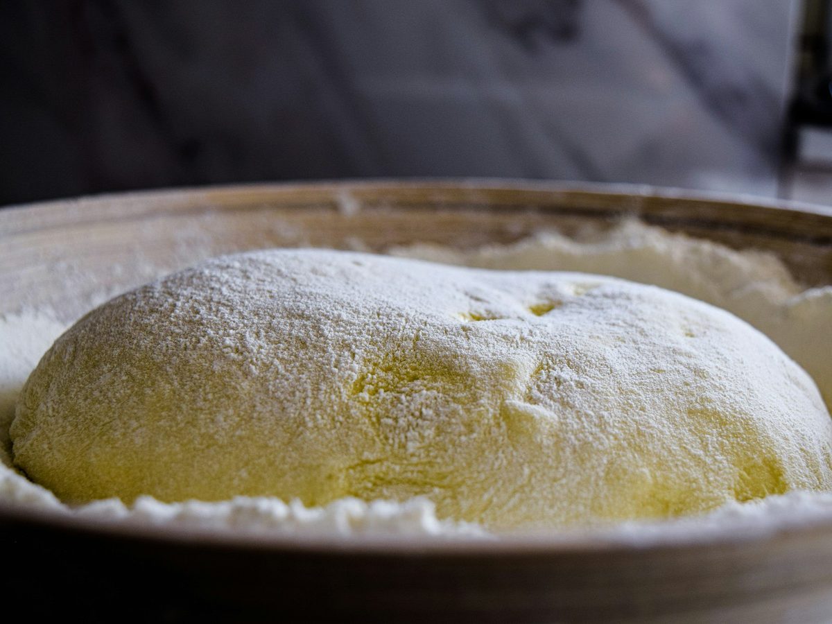A risen ball of dough dusted with flour in a bowl.