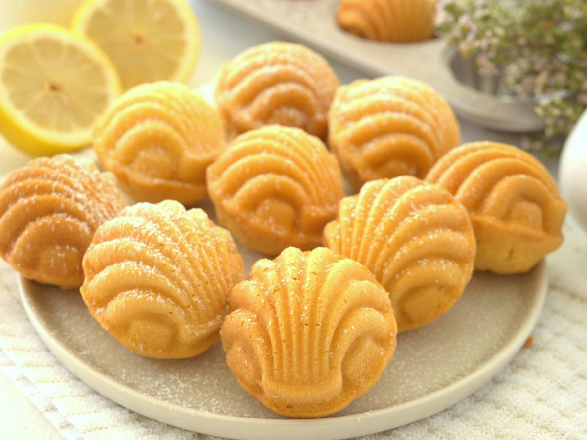 Golden shell-shaped madeleines on a plate with lemon halves.