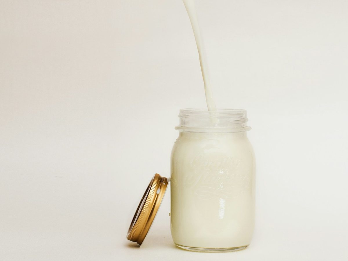 Cream being poured into a glass jar on a pale background.