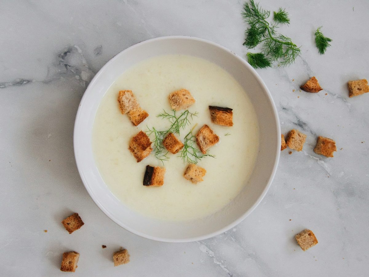 Creamy white leek and potato soup in a bowl, topped with croutons and dill.