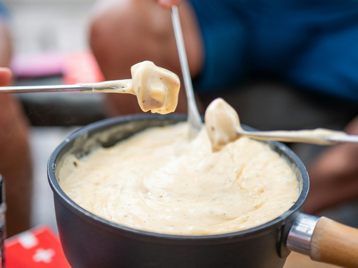A cube of bread lifted on a fork out of a pot of creamy melted cheese fondue.