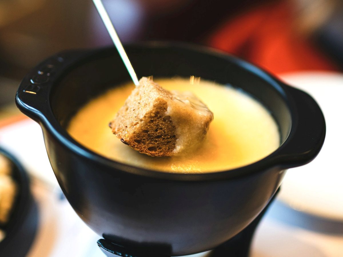 A cube of bread dipped into a black pot of melted cheese fondue.