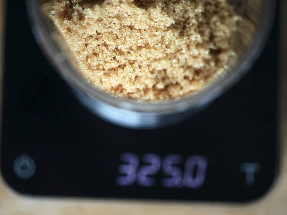 A digital kitchen scale reading 325 g under a glass jar of brown sugar.
