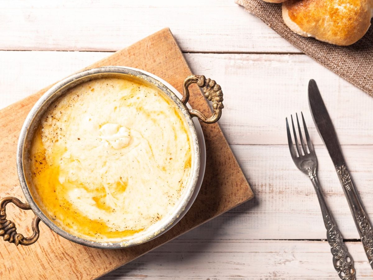 A small copper pan of creamy, whipped brandade with a drizzle of olive oil, next to bread and cutlery.
