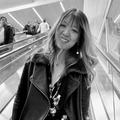 Tiffany smiling, riding down an escalator wearing a coat