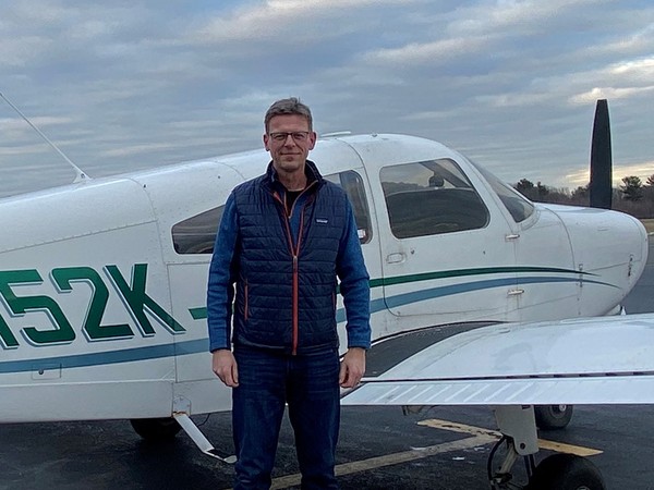 Mand med briller og blå vest står foran et hvidt propelfly.