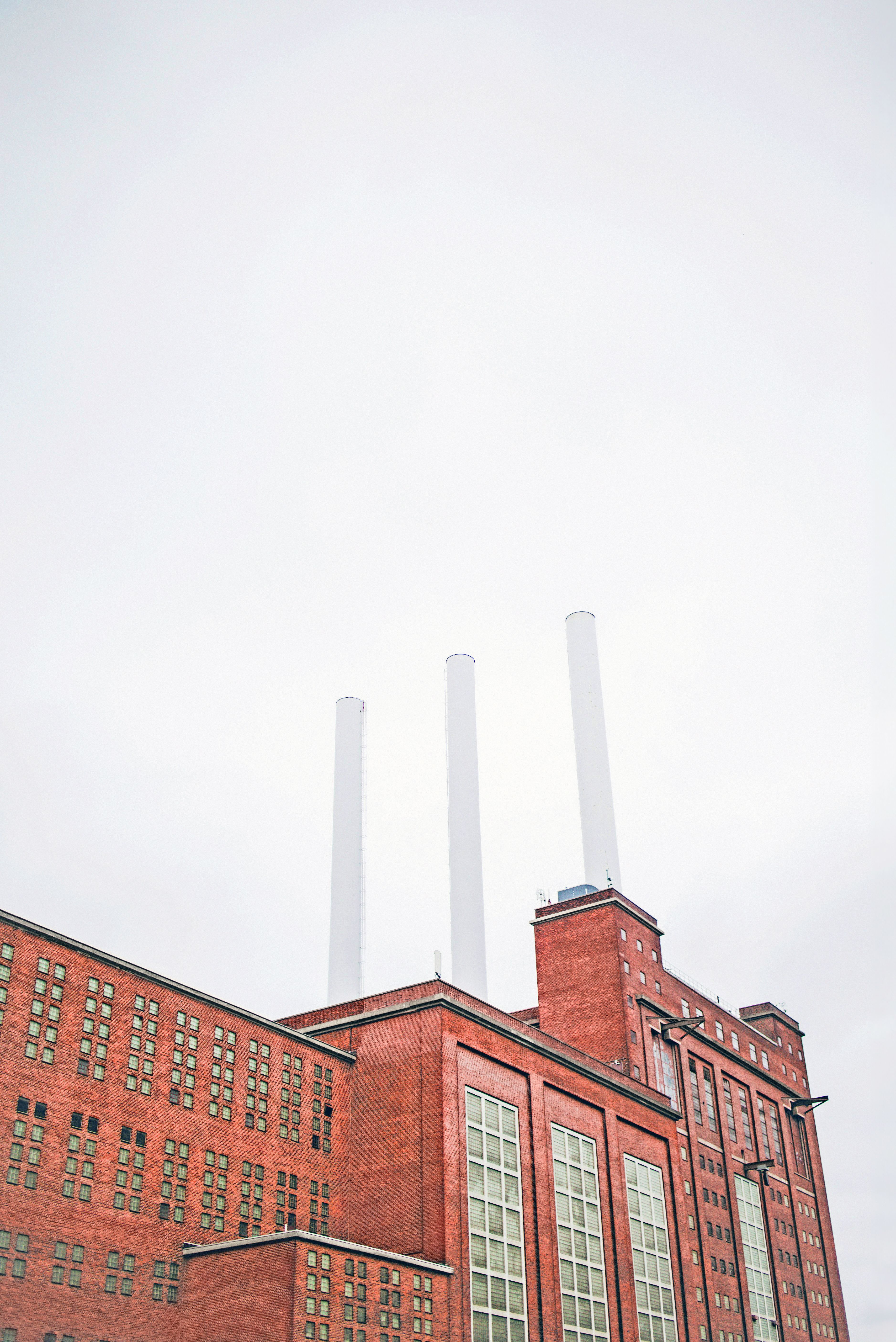 Preview of: Rød industribygning i mursten med tre høje, hvide skorstene under en overskyet himmel