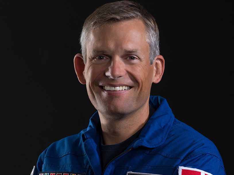 Preview of: Smilende mand med kort gråt hår i en blå astronautdragt mod sort baggrund