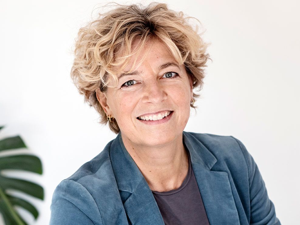 Preview of: Smilende kvinde med kort, krøllet blondt hår og blå blazer.