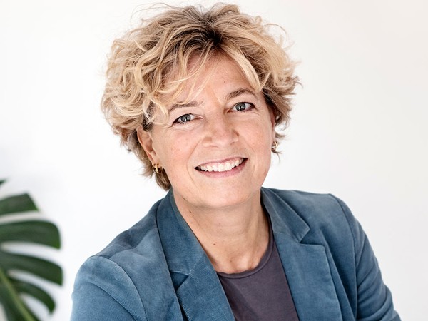 Smilende kvinde med kort, krøllet blondt hår og blå blazer.